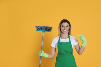 Young woman with broom on orange background, space for text