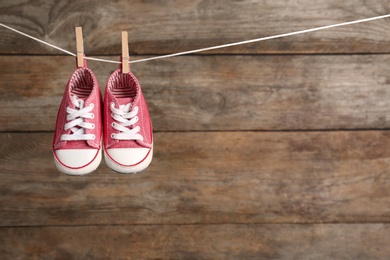 Pair of shoes on laundry line against wooden background, space for text. Baby accessories