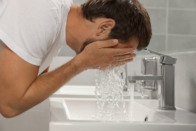 Photo of Handsome man washing face in bathroom, closeup