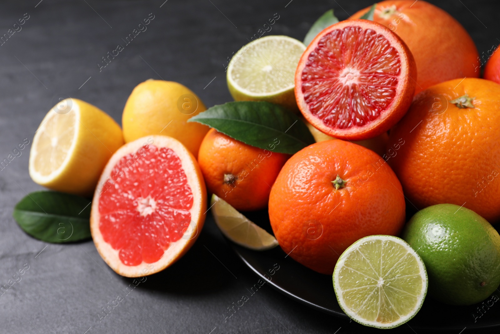 Photo of Different citrus fruits on black table, closeup