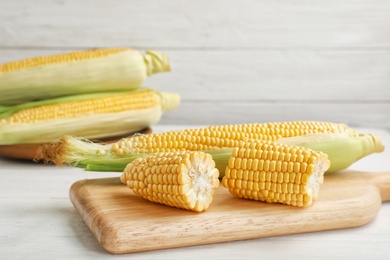 Photo of Tasty sweet corn cobs on wooden board