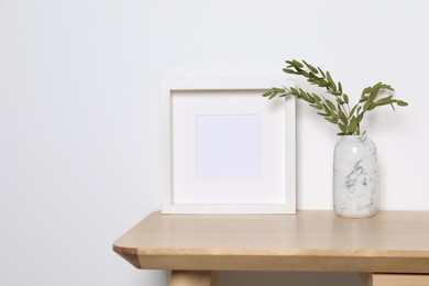 Photo of Empty photo frame and vase with decorative leaves on white table. Mockup for design