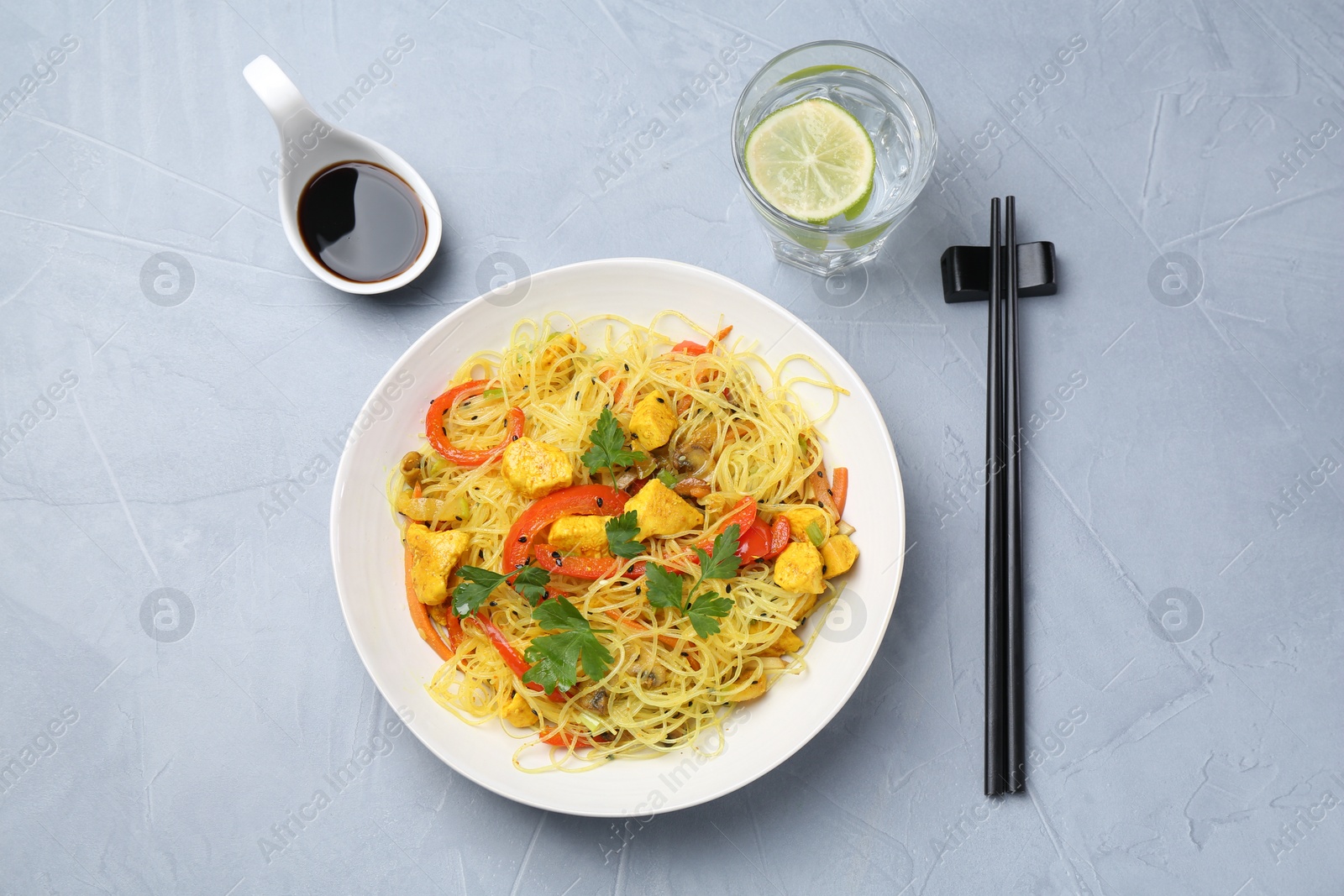 Photo of Stir-fry. Delicious cooked noodles with chicken and vegetables in bowl served on gray textured table, flat lay