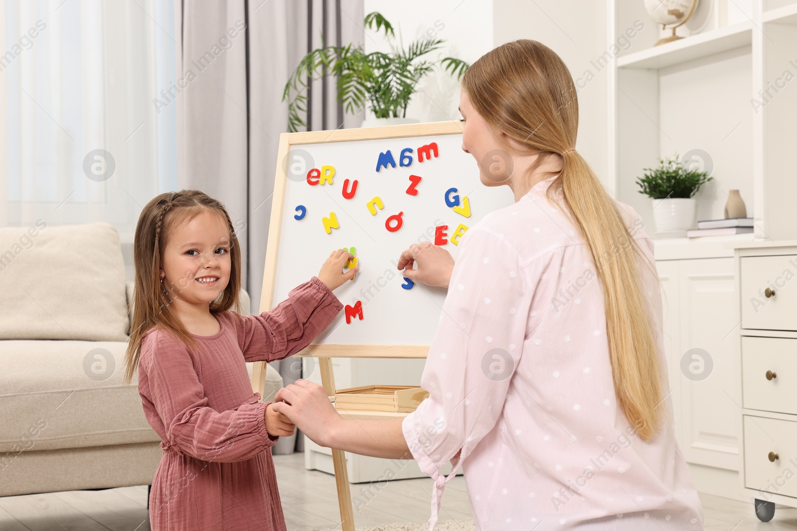 Photo of Mom teaching her daughter alphabet with magnetic letters at home