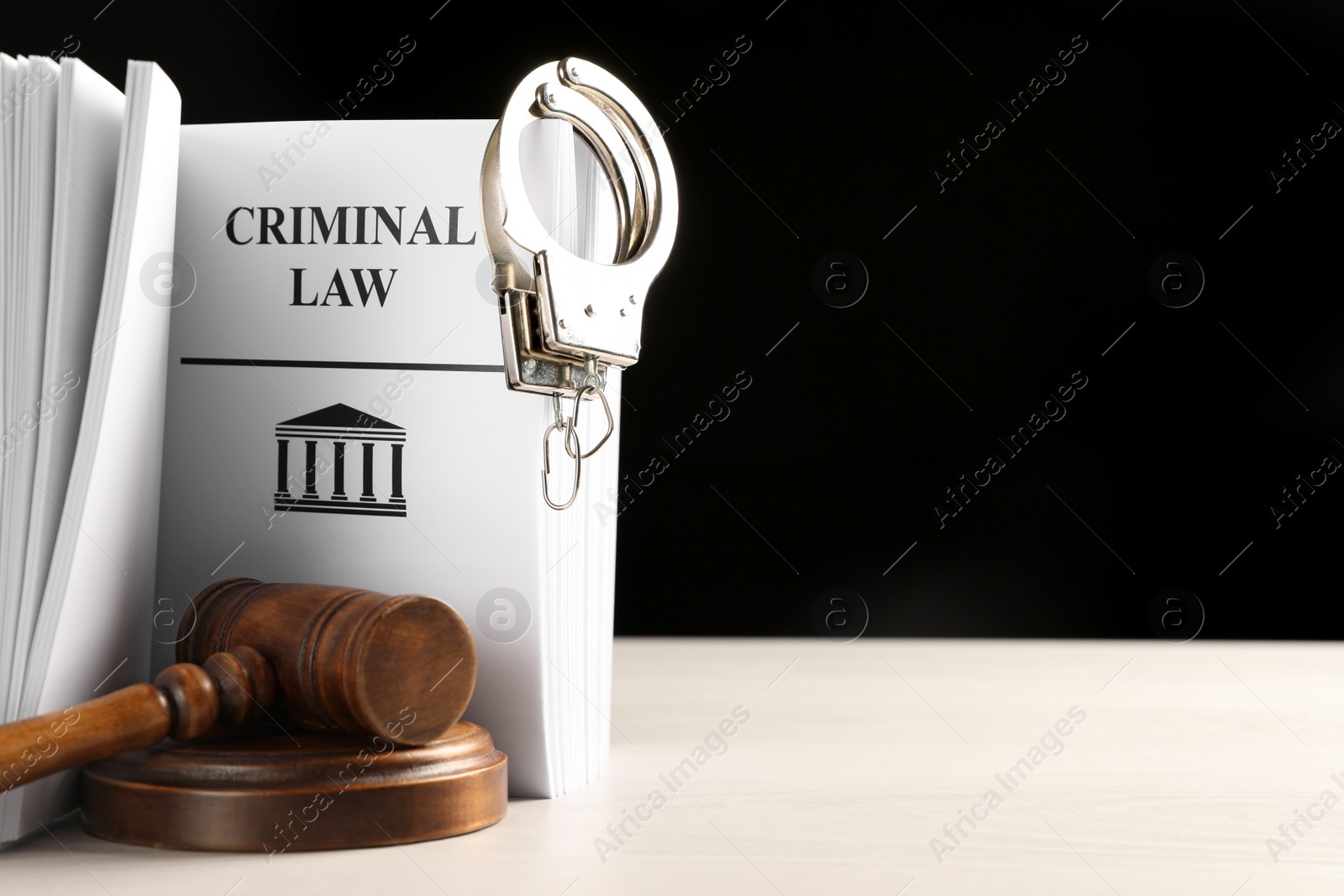 Photo of Judge's gavel, Criminal Law book and handcuffs on white table against black background. Space for text