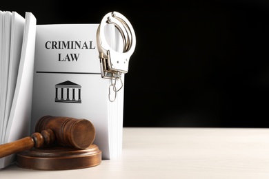 Photo of Judge's gavel, Criminal Law book and handcuffs on white table against black background. Space for text