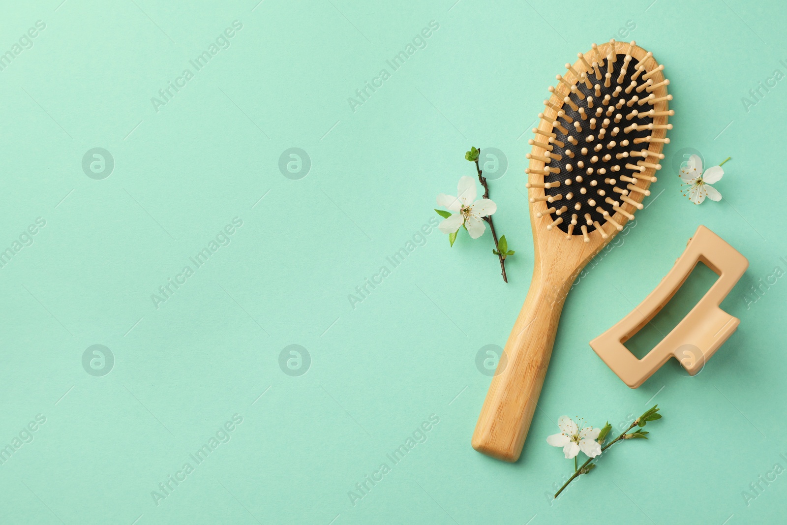 Photo of Wooden hairbrush, flower branches and barrette on turquoise background, flat lay. Space for text