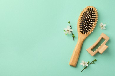 Wooden hairbrush, flower branches and barrette on turquoise background, flat lay. Space for text