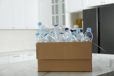 Photo of Cardboard box with used plastic bottles on table in kitchen. Recycling problem