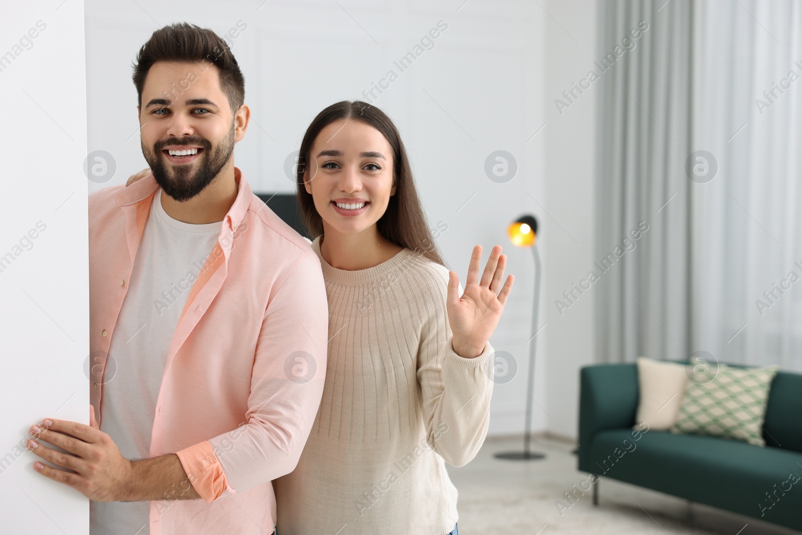 Photo of Happy couple standing near white wall at home, space for text. Invitation to come in room