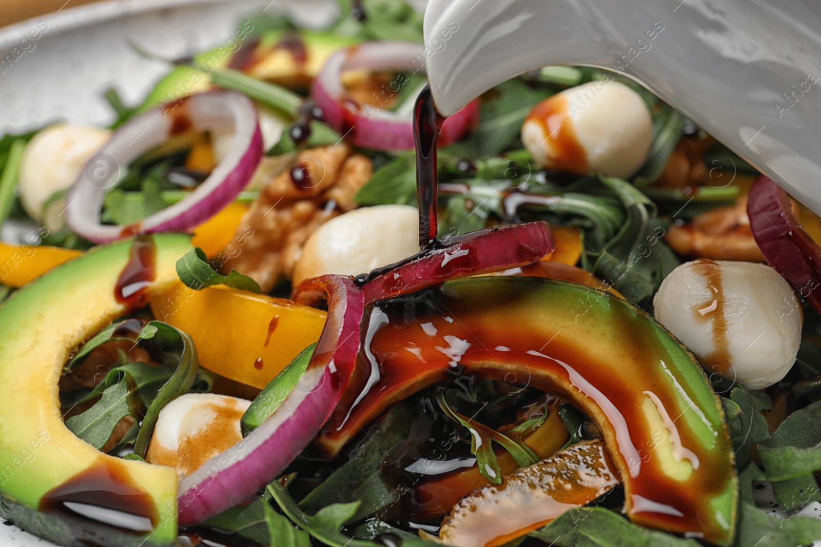 Photo of Pouring balsamic vinegar onto fresh vegetable salad, closeup