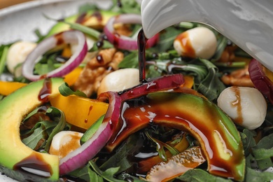 Photo of Pouring balsamic vinegar onto fresh vegetable salad, closeup