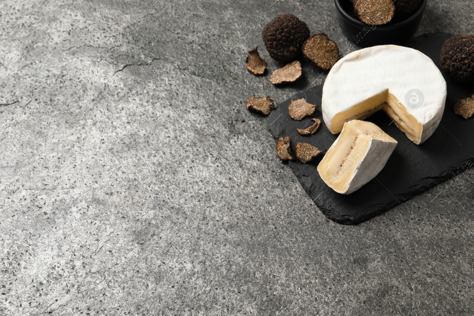 Photo of Delicious cheese and fresh black truffles on grey table. Space for text