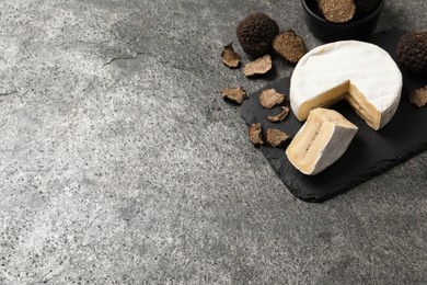 Photo of Delicious cheese and fresh black truffles on grey table. Space for text