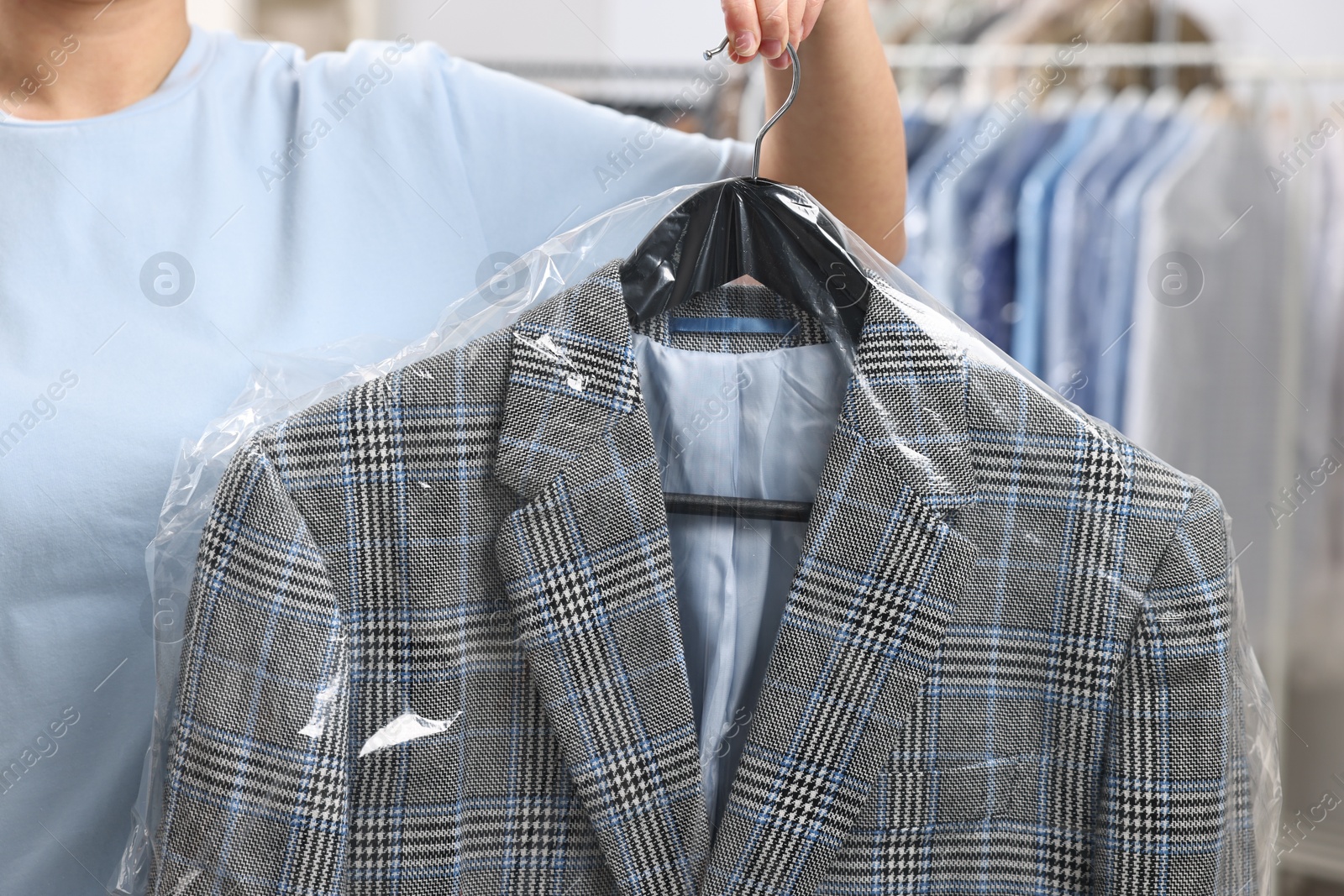 Photo of Dry-cleaning service. Woman holding jacket in plastic bag indoors, closeup