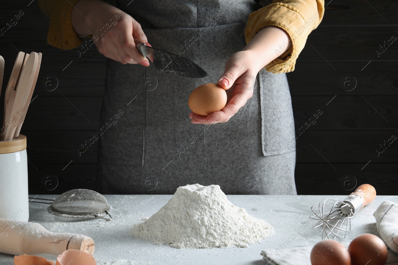 Photo of Woman beating egg into dough at table on dark background, closeup