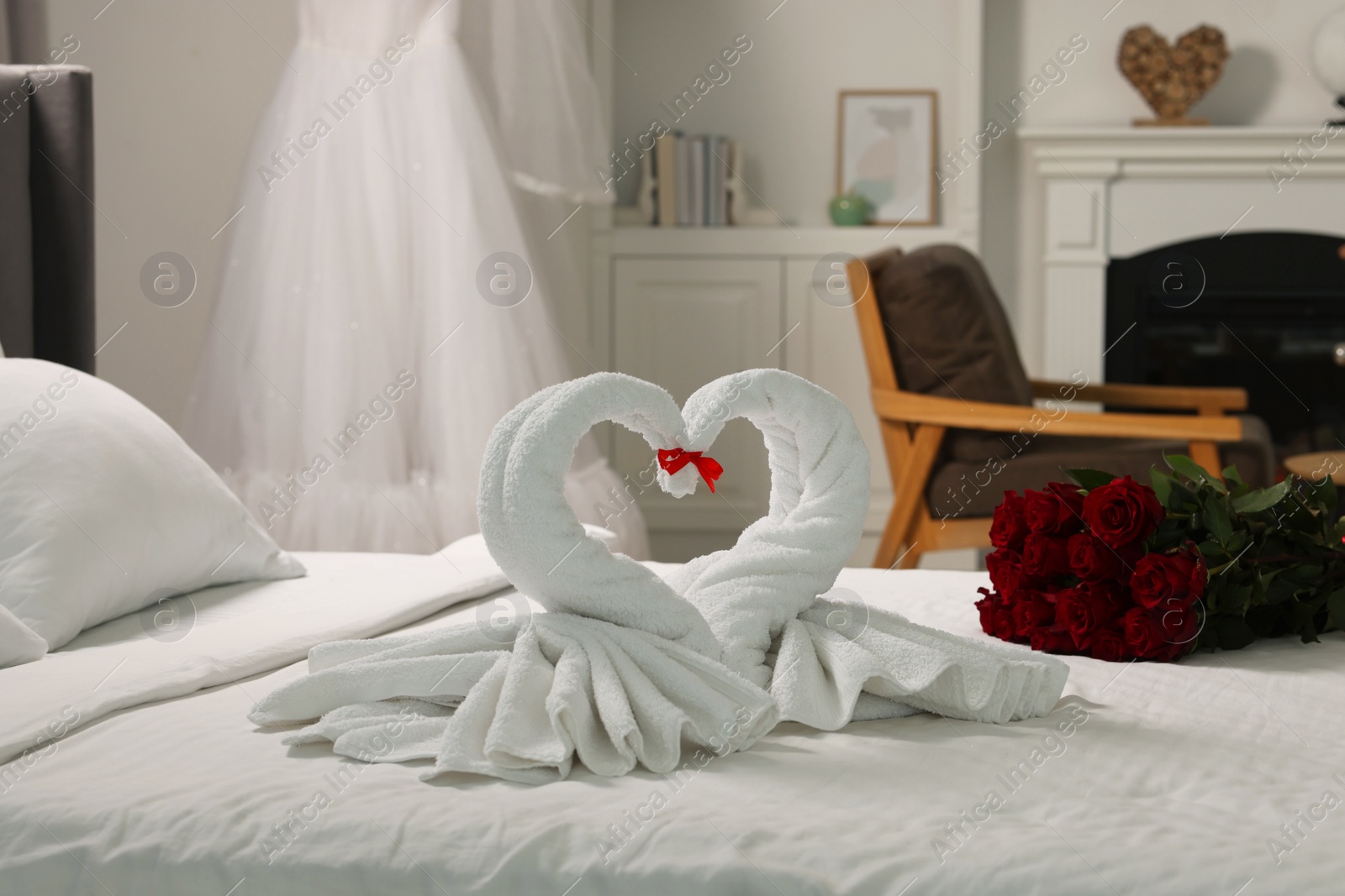 Photo of Honeymoon. Swans made of towels and beautiful red roses on bed in room