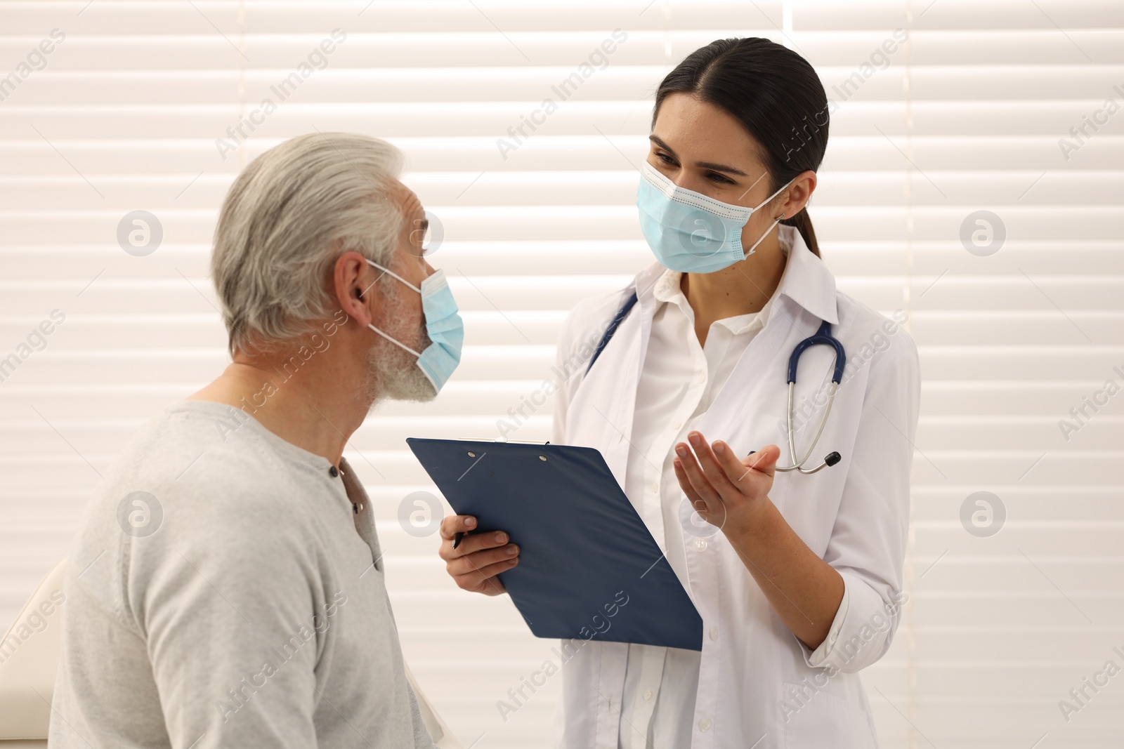 Photo of Nurse with clipboard talking to elderly patient indoors