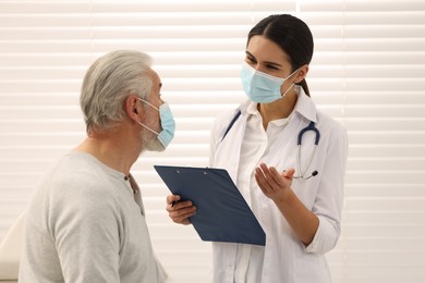 Nurse with clipboard talking to elderly patient indoors
