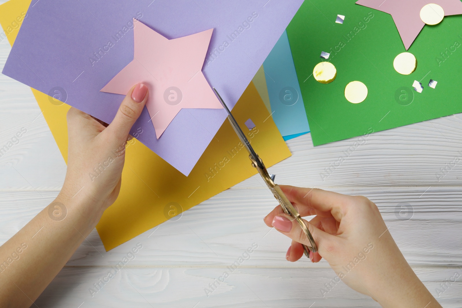 Photo of Woman cutting paper star with scissors at white wooden table, top view