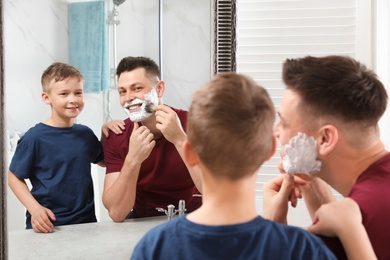 Photo of Dad applying shaving foam near son at mirror in bathroom