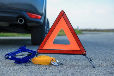 Photo of Emergency warning triangle, towing strap and scissor jack near car outdoors. Safety equipment