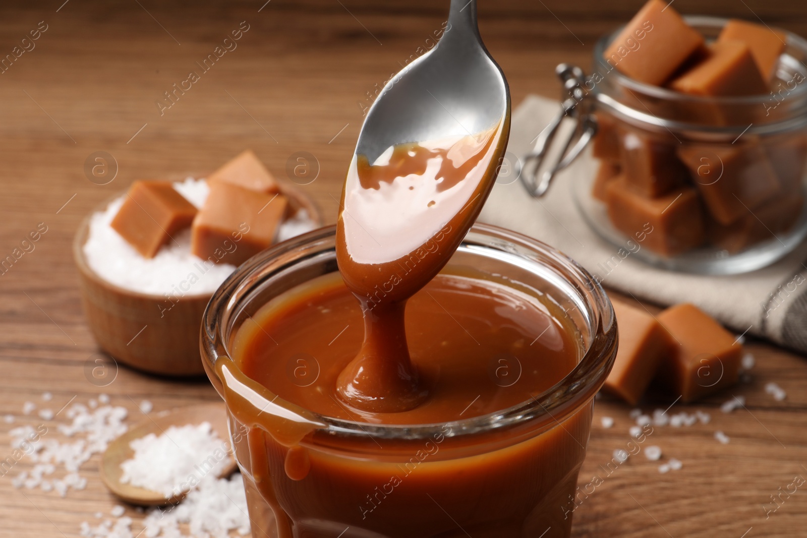 Photo of Taking tasty salted caramel with spoon from glass, closeup