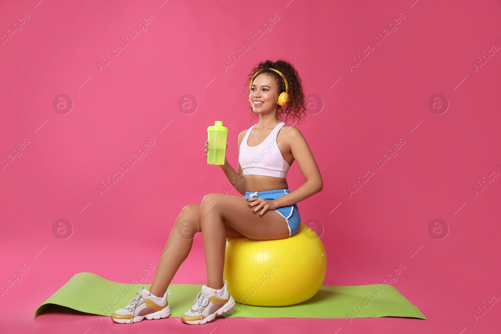 Photo of Beautiful African American woman with headphones  on yoga mat against pink background