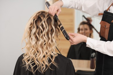 Photo of Hair styling. Hairdresser curling woman's hair in salon, closeup