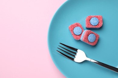 Photo of Light blue plate with fork and dishwasher detergent tablets on pink background, top view. Space for text