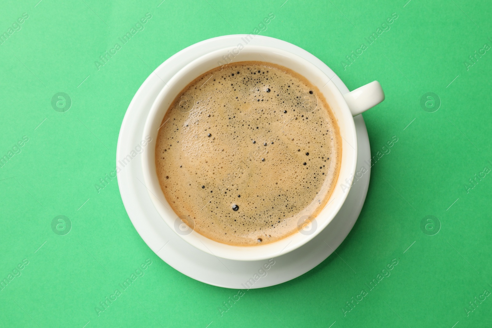 Photo of Aromatic coffee in cup on green background, top view