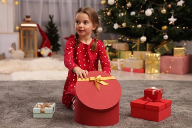 Photo of Cute little child with gift boxes near Christmas tree at home