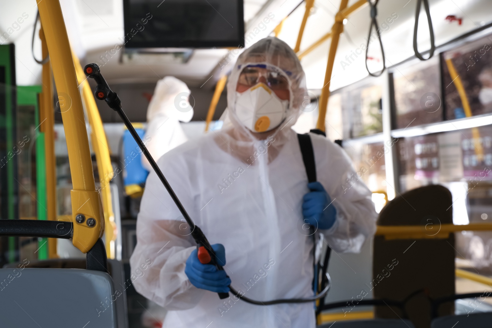 Photo of Public transport sanitation. Worker in protective suit disinfecting bus salon, focus on spray machine nozzle