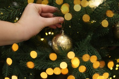 Photo of Woman decorating fir tree with golden Christmas ball, closeup