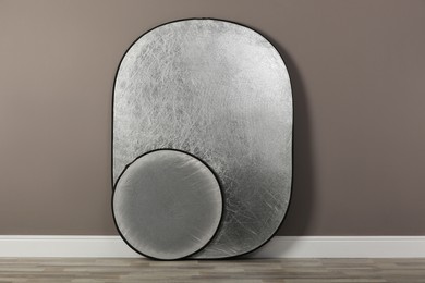 Professional silver reflectors near grey wall in room. Photography equipment
