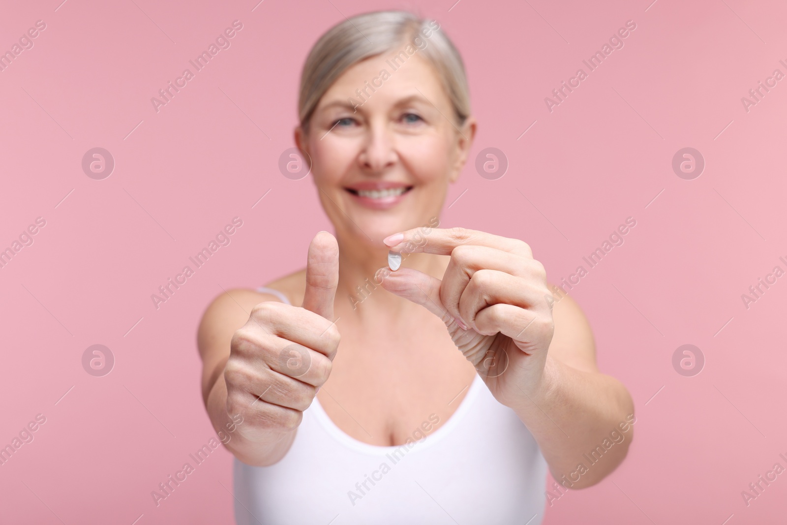 Photo of Beautiful woman with vitamin pill showing thumbs up on pink background, selective focus