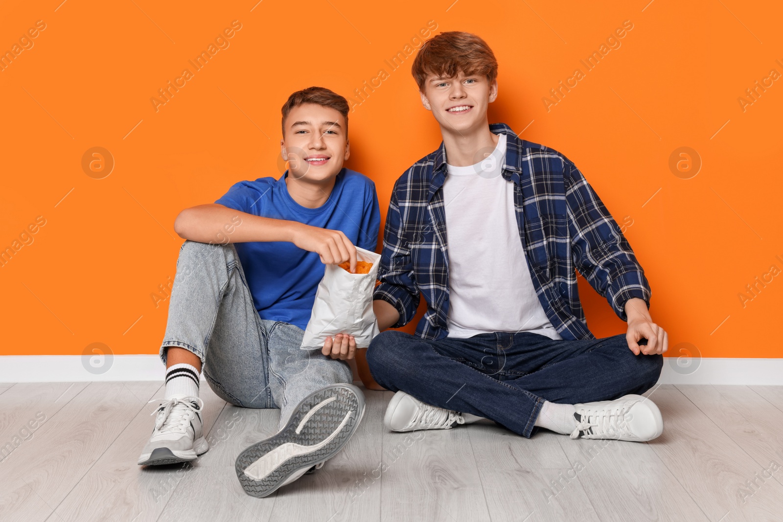 Photo of Happy teenage boys eating chips near orange wall