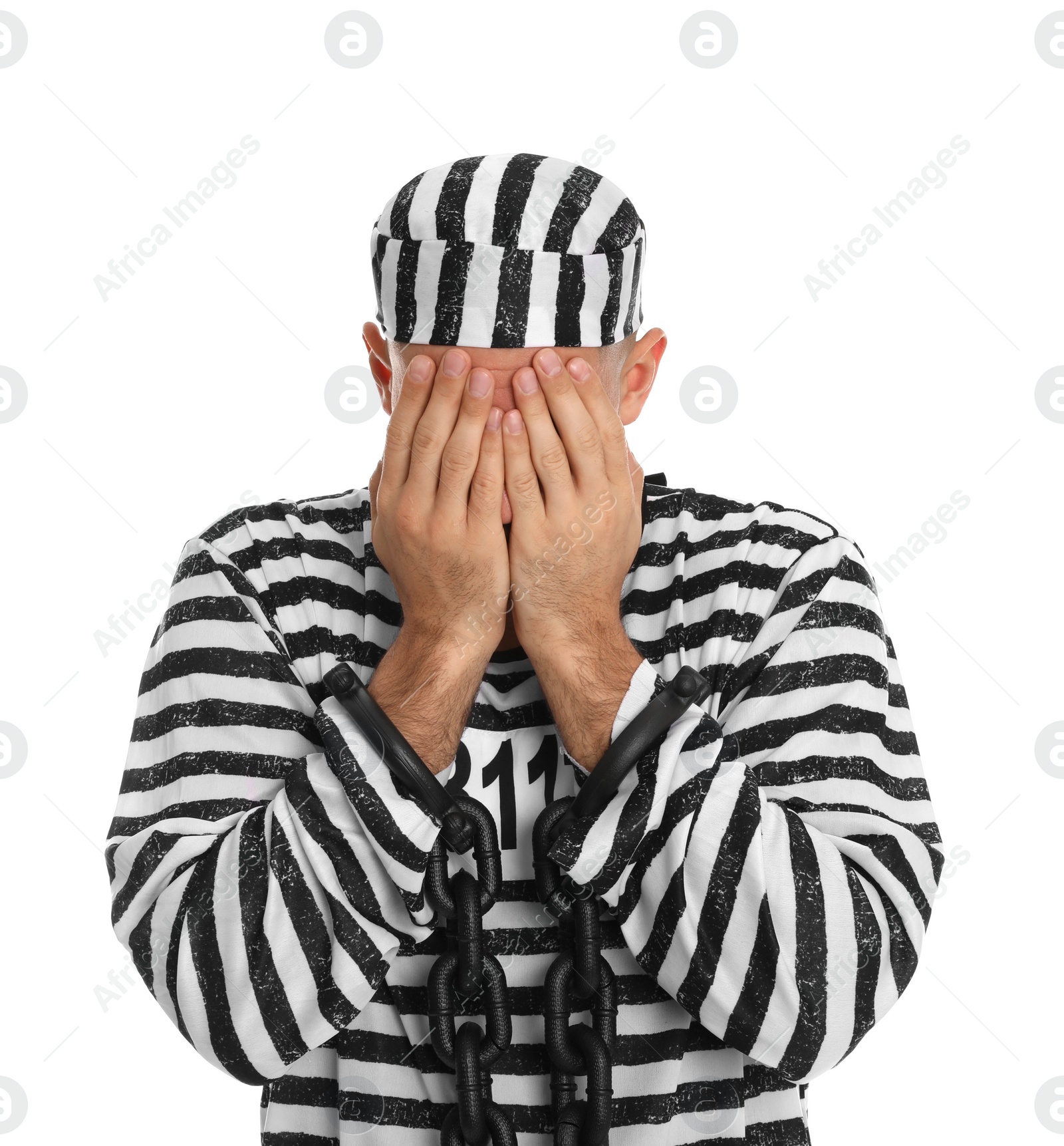 Photo of Remorseful prisoner in striped uniform with chained hands hiding his face on white background