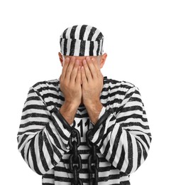 Remorseful prisoner in striped uniform with chained hands hiding his face on white background