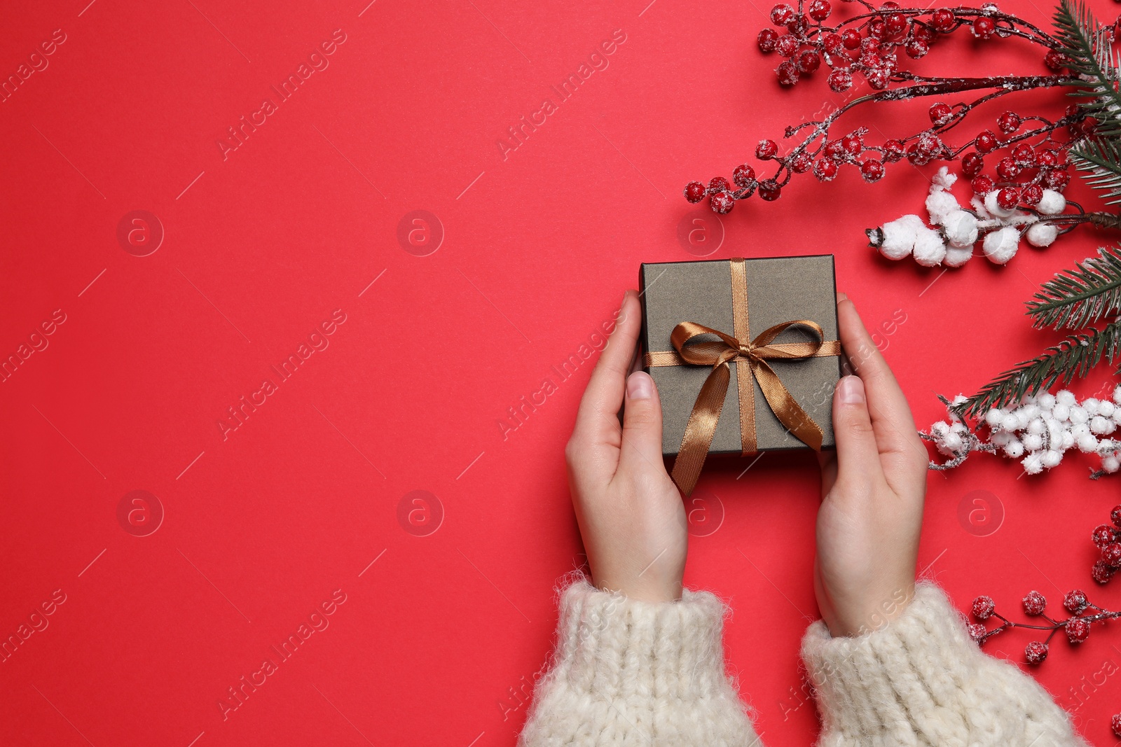 Photo of Woman with Christmas gift and decorative branches on red background, top view. Space for text