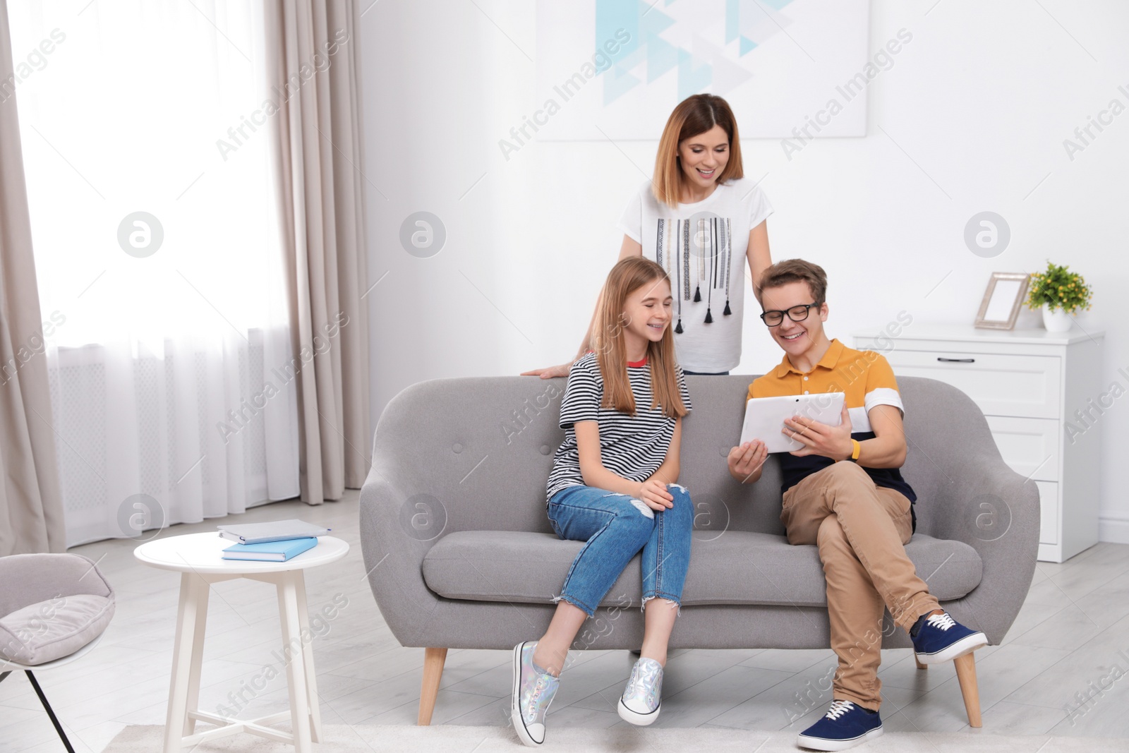 Photo of Happy mother, her teenager daughter and son with tablet at home