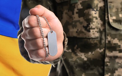 Image of Closeup view of soldier in uniform holding military ID tag and Ukrainian flag on background