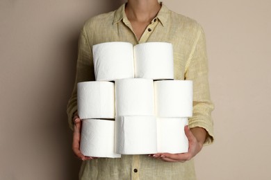 Woman with heap of toilet paper rolls on beige background, closeup