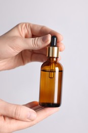 Photo of Woman holding bottle of cosmetic oil on light background, closeup