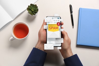 Image of Spam warning message, envelope illustrations popping out of device display. Man using email software on smartphone at table, top view