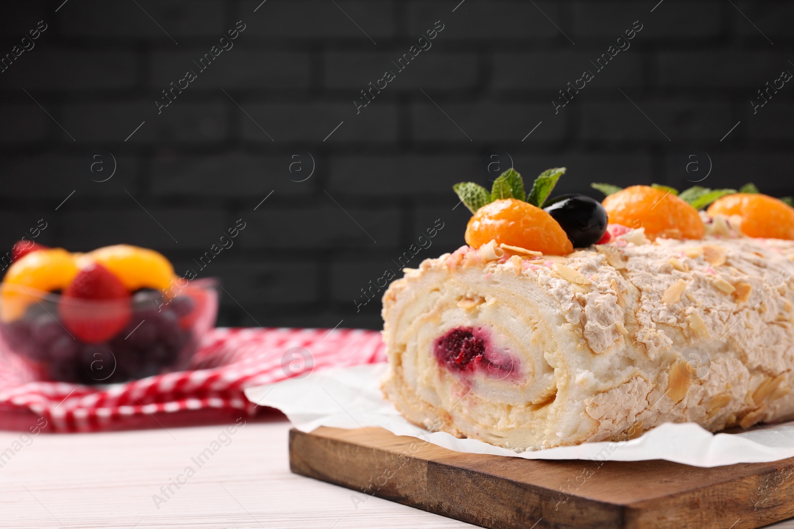 Photo of Tasty meringue roll with jam, tangerine slices and mint leaves on white wooden table, closeup. Space for text