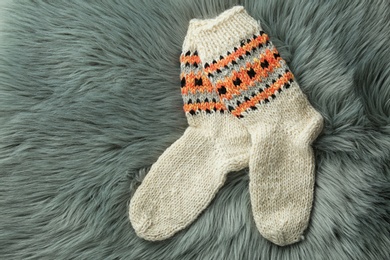 Photo of Knitted socks on grey faux fur, flat lay. Space for text