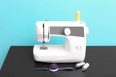 Photo of Modern sewing machine on table against color background