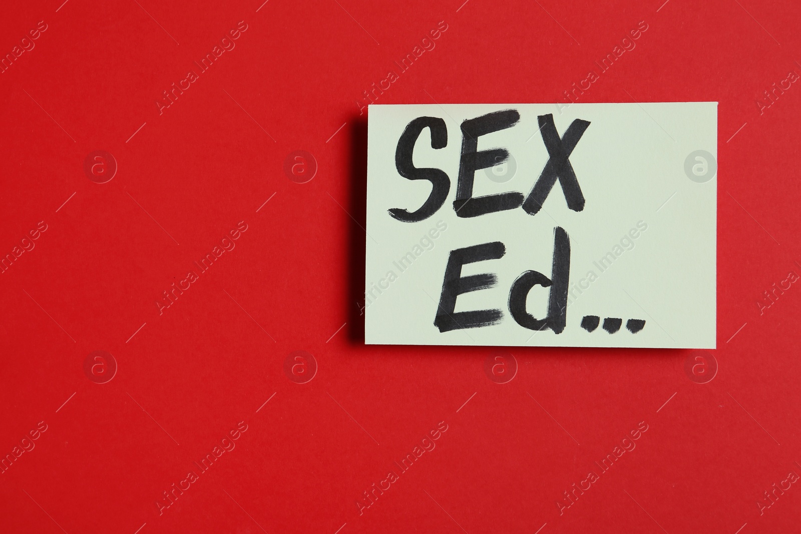 Photo of Piece of paper with text "SEX ED..." on red background, top view. Space for text