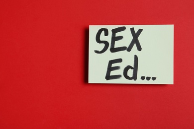 Photo of Piece of paper with text "SEX ED..." on red background, top view. Space for text